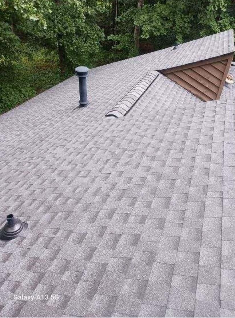 Gray shingle roof with two vents and a ridgeline. Lush green trees in the background create a serene and natural atmosphere.