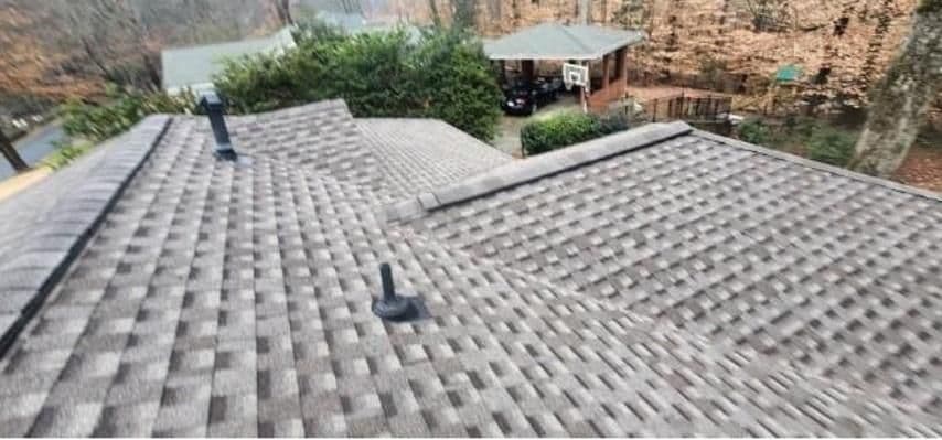 Aerial view of a shingled roof with attic vents. Autumn trees and a patio with a basketball hoop and parked car are visible in the background.