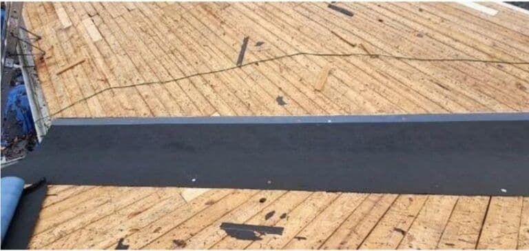 A plywood roof under construction with scattered debris is partially covered by a wide strip of black waterproof underlayment, suggesting ongoing work.