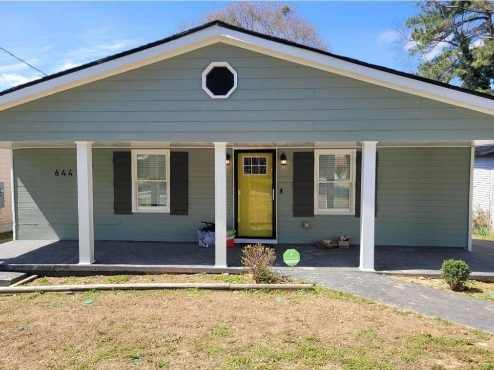 A cozy house with light blue siding and a yellow front door. The porch is supported by white columns. A small, dry front lawn is in the foreground.